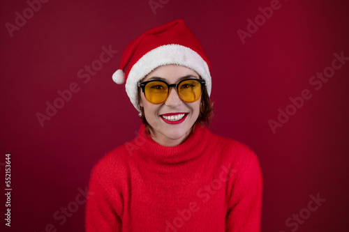 Young positive woman in christmas santa hat isolated over redl background. Happy young woman in Santa s helper hat a red background.