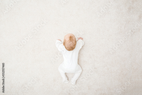 Canvastavla Baby in white bodysuit crawling on knee and arms on light beige home carpet
