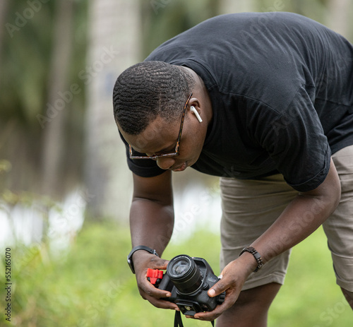 Portrait of a young black African photographer unpacking his photography equipment, a tripod, in a West African village during an outdoor photo shoot