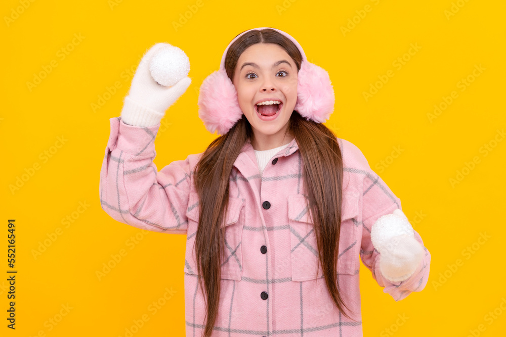 amazed child in fur earmuffs playing snowballs on yellow background, winter amazed child in fur earmuffs playing snowballs on yellow background, winter