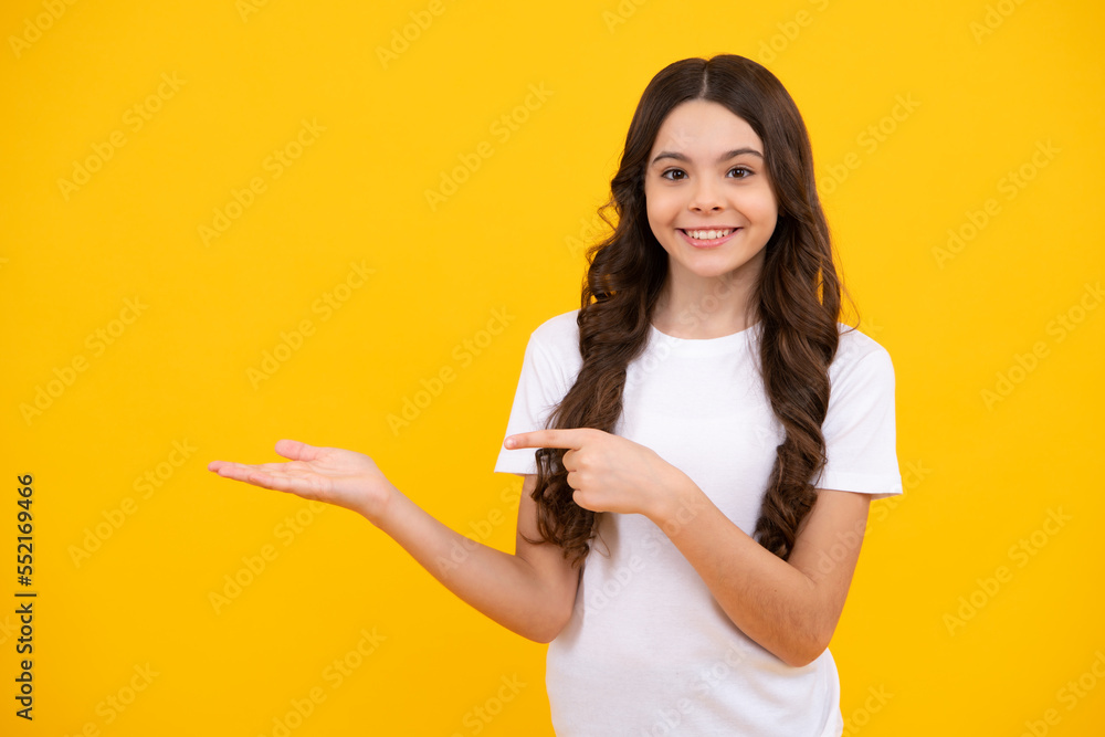 Look at advert. Teenager child points aside shows blank copy space for text promo idea presentation, poses against yellow background. Happy teenager, positive and smiling emotions of teen girl. Look at advert. Teenager child points aside shows blank copy space for text promo idea presentation, poses against yellow background. Happy teenager, positive and smiling emotions of teen girl.
