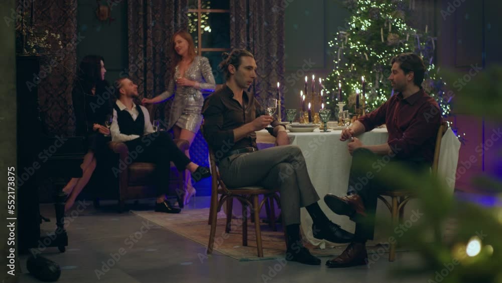 Good looking and handsome two men celebrating together with friends Christmas or New Year they sitting at the Christmas dining table discussing while other friends sitting on the background on the Good looking and handsome two men celebrating together with friends Christmas or New Year they sitting at the Christmas dining table discussing while other friends sitting on the background on the
