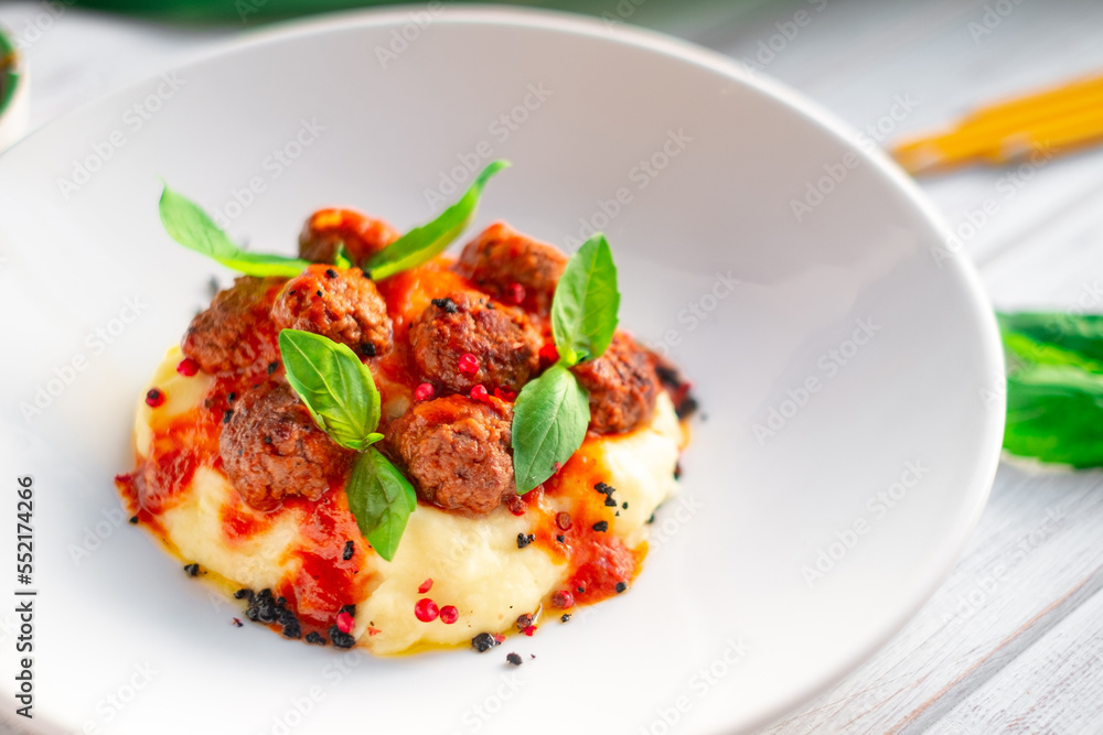 Beef meatballs in tomato sauce with mashed potatoes and basil in a white plate