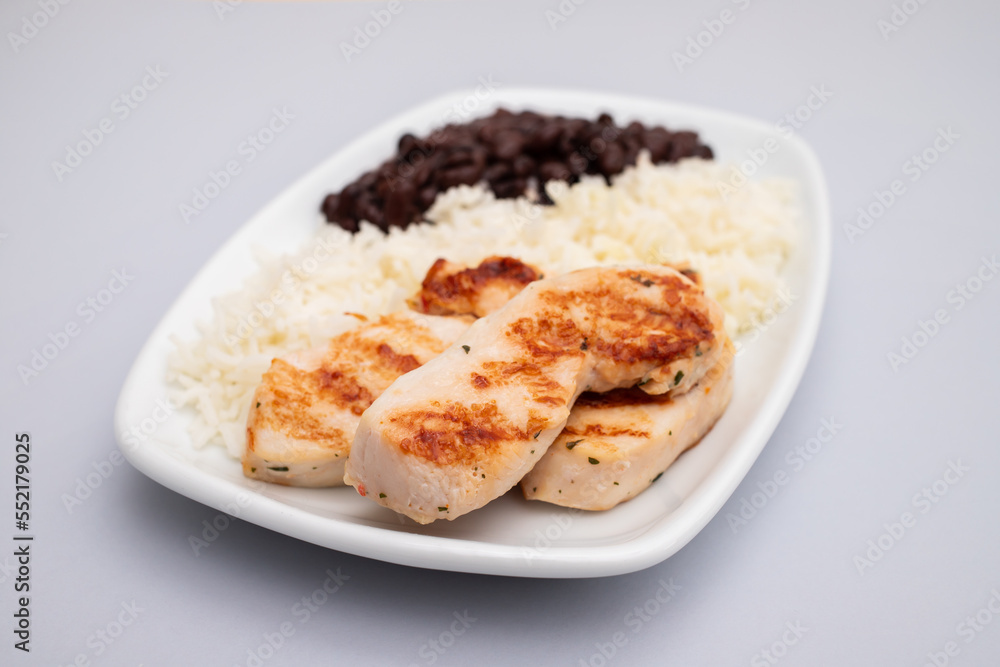 Healthy food with chicken breast, beans and rice on a white plate.