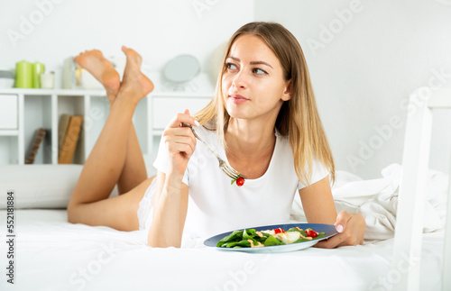 Cheerful young girl in lingerie having a salad while laying in the bed. High quality photo