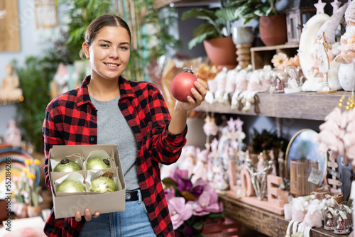 Portrait of positive woman choosing christmas tree balls on sale in store