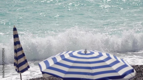 striped sun umbrellas on the background of azure sea waves on a sunny day, pebble beach, sun glare