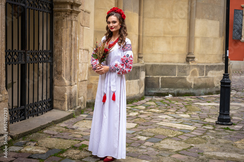 Portrait of a beautiful Slavic girl with long blond hair and blue eyes with a flower crown in a white and red embroidered dress with a bouquet. Traditional clothes of the Ukrainian region © Jurii