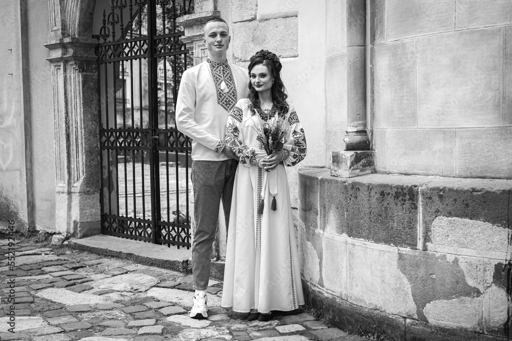 Black and white portrait. A happy young couple in love, a family walking through the old city of Lviv in Ukrainian embroidered dresses, holding hands. Young people hug in the old town of Lviv Black and white portrait. A happy young couple in love, a family walking through the old city of Lviv in Ukrainian embroidered dresses, holding hands. Young people hug in the old town of Lviv
