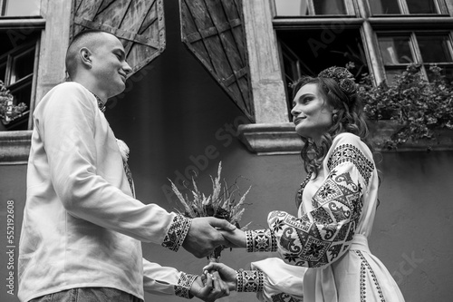 Black and white portrait. A happy young couple in love, a family walking through the old city of Lviv in Ukrainian embroidered dresses, holding hands. Young people hug in the old town of Lviv