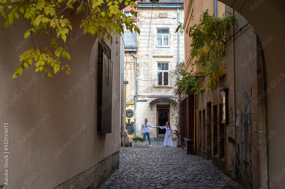 A happy young couple in love, a family walking through the old city of Lviv in Ukrainian embroidered dresses, holding hands. Young people hug in the old town of Lviv
