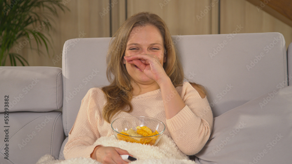 CLOSE UP: Smiling woman sitting on comfortable sofa and watching TV comedy CLOSE UP: Smiling woman sitting on comfortable sofa and watching TV comedy
