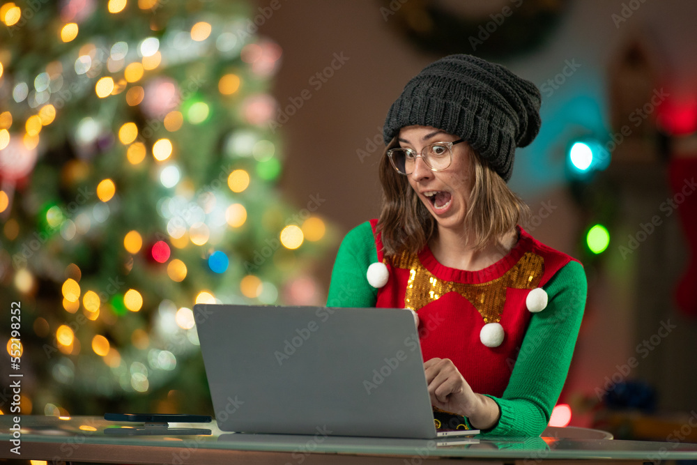 Excited young woman using a laptop computer in front of a Christmas Tree in her living room. Excited young woman using a laptop computer in front of a Christmas Tree in her living room.