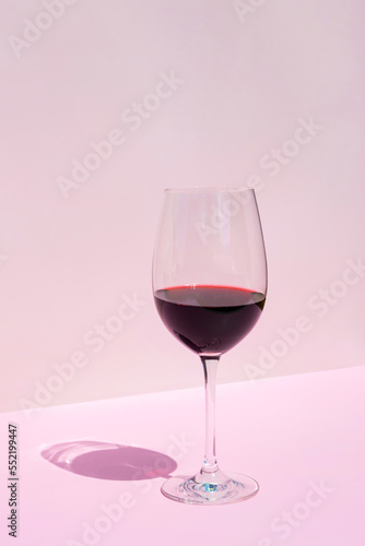 Wine glass with red wine on a pink background in the rays of the bright sun. Place for text