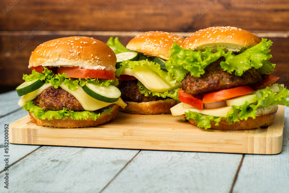 Delicious burgers with lettuce and cheese served on cutting board Delicious burgers with lettuce and cheese served on cutting board