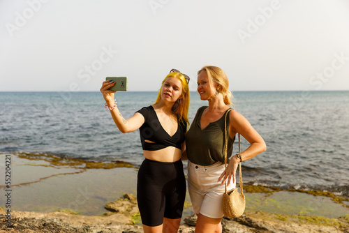 Mother and daughter take selfies against the backdrop of the sea
