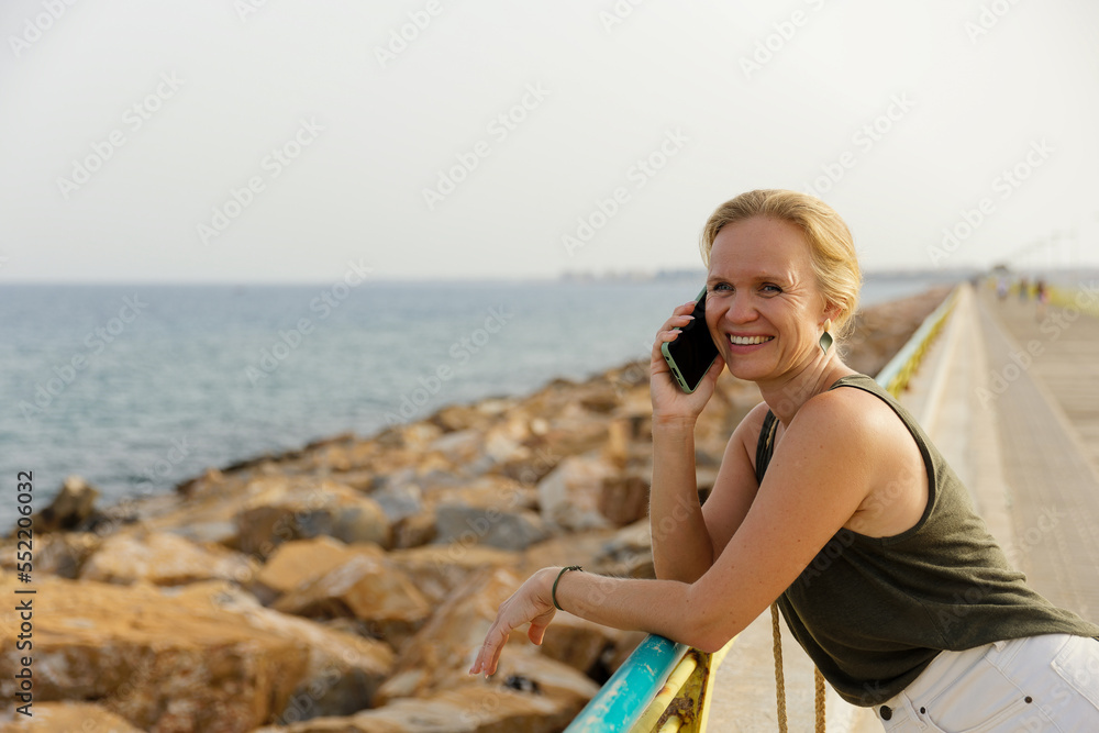 A young stylish woman communicates on a smartphone on the city embankment, Rest and work in nature, by the sea