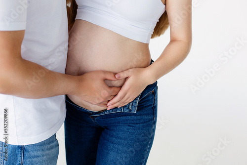 A pregnant woman and a loving husband hugs her stomach on a white background. The feeling of the baby's movement by a couple on the pregnant woman's stomach. Close-up.