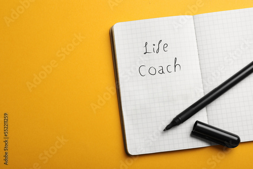 Phrase Life Coach written in notebook and marker on yellow background, top view. Space for text