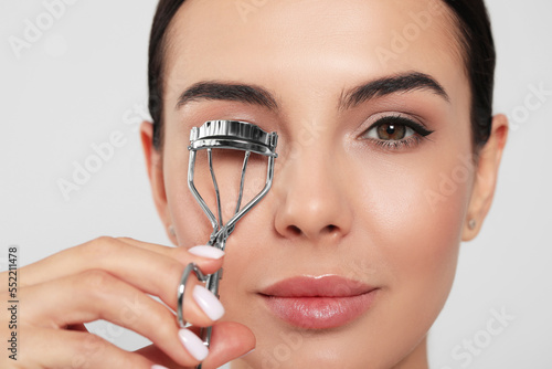 Fotografia Beautiful young woman using eyelash curler on white background, closeup