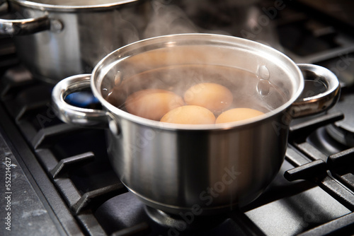 Jajka gotujące się w małym garnuszku ze stali nierdzewnej na czarnej kuchence gazowej