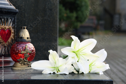 White lilies and grave light on grey granite tombstone outdoors. Funeral ceremony