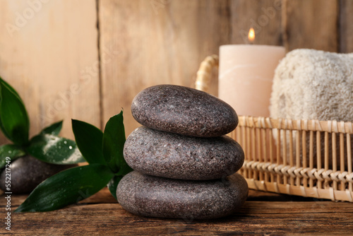 Stacked spa stones, bamboo leaves, candle and towel on wooden table. Space for text