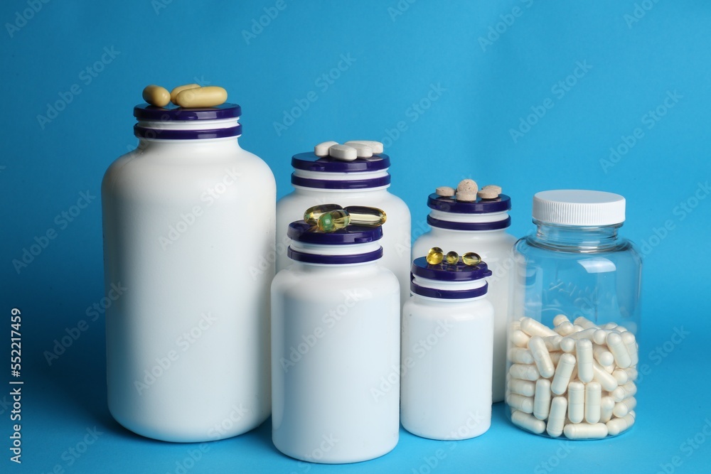 White medical bottles and different pills on light blue background White medical bottles and different pills on light blue background