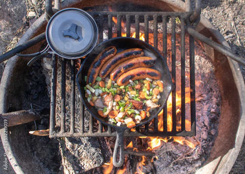 That Smokey Flavor of Breakfast Over a Campfire.Sausage, potatoes, peppers, and onions fired in a cast iron pan.A pot and a pan over a campfire at a campground