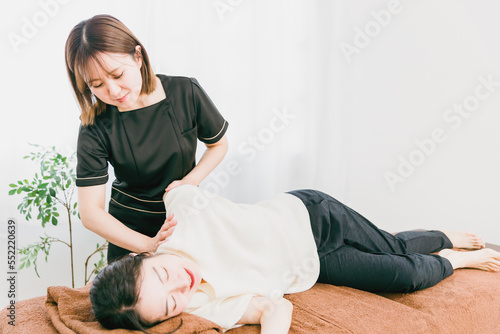 肩のマッサージをするマッサージ師・カイロプラクター・セラピスト・整体師・理学療法士のアジア人女性 