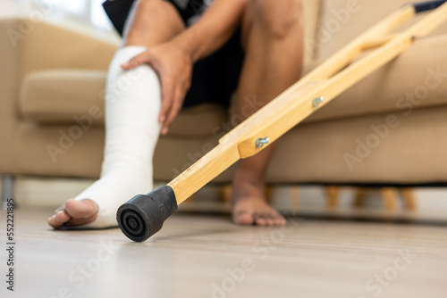 Man suffer pain from accident fracture broken bone injury with leg splints in cast neck splints collar sling support arm walking at home with crutch. Social security and health insurance concept.