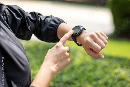 Woman checking sports smart watch in the city at sunrise. Asian female adjusting smart watch before workout outdoor. Exercise in the morning. Healthy and technology lifestyle concept.