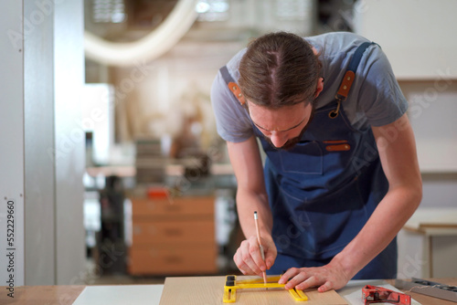 Happy caucasian white carpenter using a professional ruler measures and pencil to making a mark on wood panel. Professional carpenter measuring a wood plank.