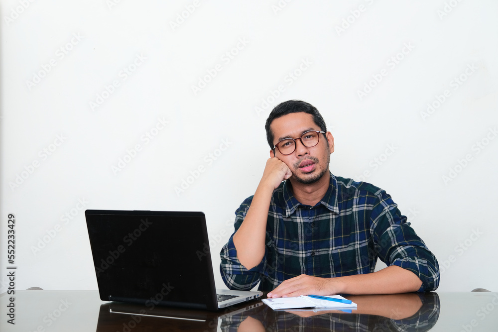 Adult Asian man sitting in his working desk with lazy gesture Adult Asian man sitting in his working desk with lazy gesture