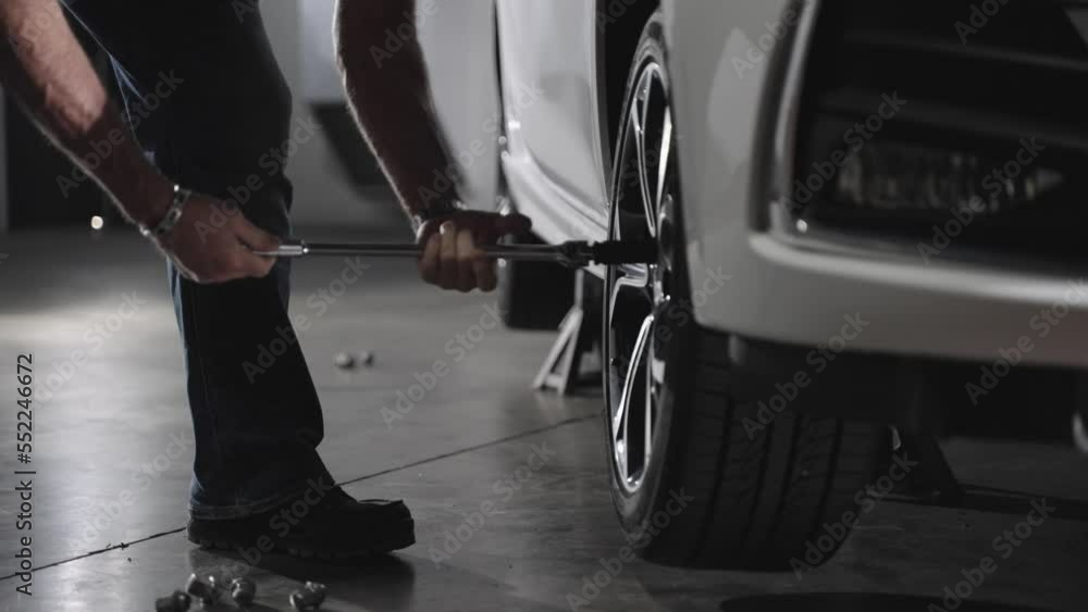 Unrecognizable mechanic removing lug nuts from car wheel with lug wrench, slow motion Unrecognizable mechanic removing lug nuts from car wheel with lug wrench, slow motion