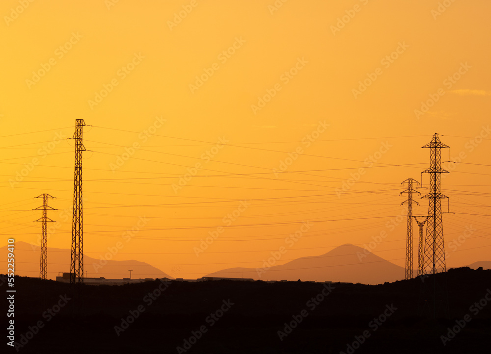 Calima, sand storm in Lanzarote. View of Volcanoes and electricity transmission pylons silhouetted against orange sky. Costa Teguise, Canary Islands, Spain.
