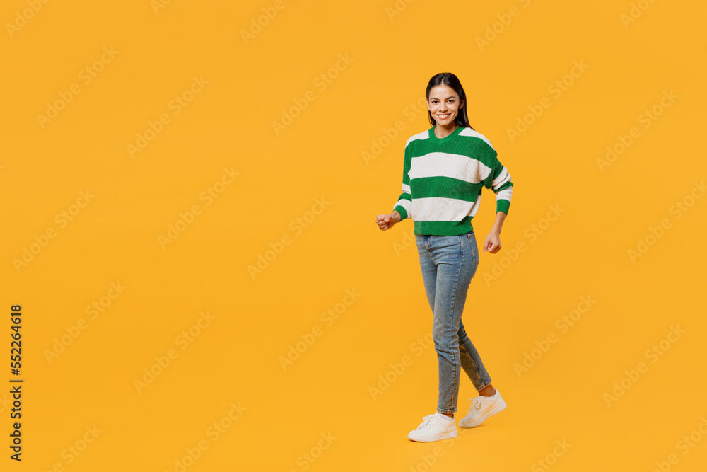 Full body side view smiling happy young latin woman wear casual cozy green knitted sweater walk go strolling look camera isolated on plain yellow background studio portrait People lifestyle concept. Full body side view smiling happy young latin woman wear casual cozy green knitted sweater walk go strolling look camera isolated on plain yellow background studio portrait People lifestyle concept.