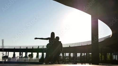 A man in a chair for people with physical disabilities and a woman dancing at sunset.