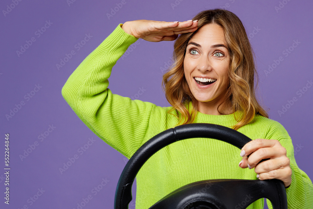 Young happy woman 30s wearing casual green knitted sweater hold steering wheel driving car hold hand at forehead look asidfar away distance isolated on plain pastel purple background studio portrait. Young happy woman 30s wearing casual green knitted sweater hold steering wheel driving car hold hand at forehead look asidfar away distance isolated on plain pastel purple background studio portrait.