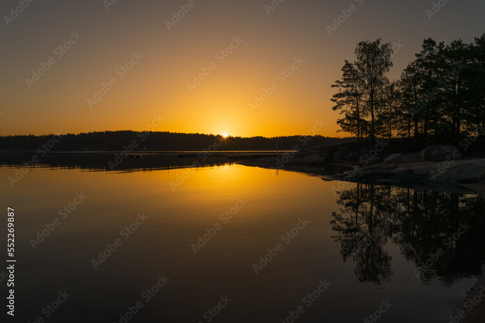 A golden-orange sunset on the sea with a silhouette of a tree line on the horizon. Nature of Finland. Scandinavia. Natural background. Space for text.