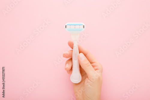 Young adult woman hand holding razor on light pink table background. Pastel color. Closeup. Female product for smooth body skin. Top down view. photo