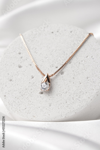 Fototapeta Golden necklace with crystals on concrete podium on white silk background, rose gold, single diamond pendant