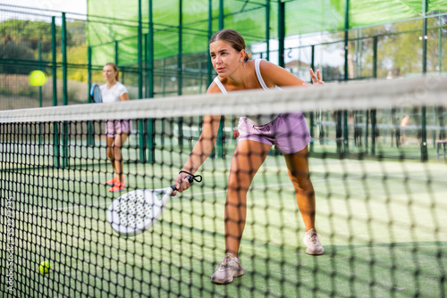 Caucasian young woman in tank top and shorts playing padel tennis match during training on court.