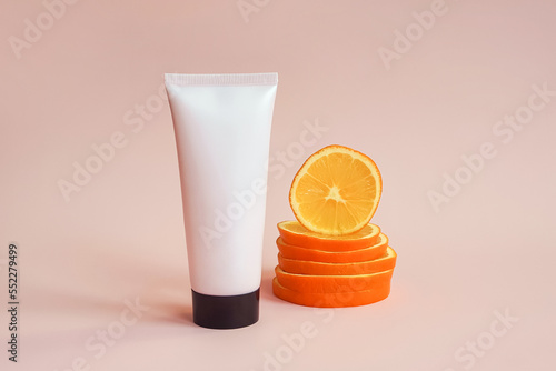 Mockup pink squeeze bottle cosmetic tube with screw black cap and orange slices on pink background. Lotion, moisturizer, balsam, hand cream, gel, skincare with vitamin c. Mock-up, front view photo