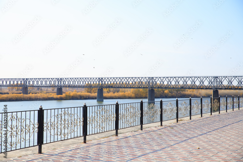 River embankment and Railway bridge over river on sunny autumn day. Selective focus