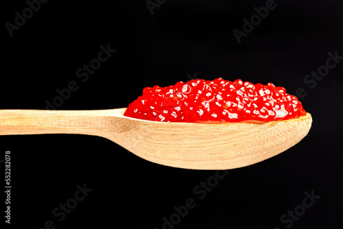 Delicious red caviar in wooden spoon on black background