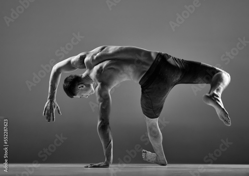 Black and white footage of male flexible muscular athlete showing animal flow sport elements isolated over gray background. Fitness, trendy sports, beauty of body photo