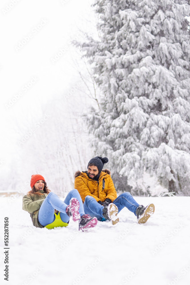 Couple sliding down the hill in the snow while on winter vacation
