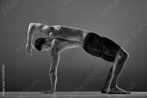 Black and white footage of male flexible muscular athlete showing animal flow sport elements isolated over gray background. Fitness, trendy sports, beauty of body