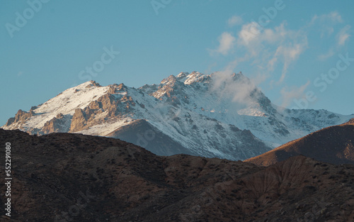 A snow-covered mountain in the rays of sunset against a blue sky